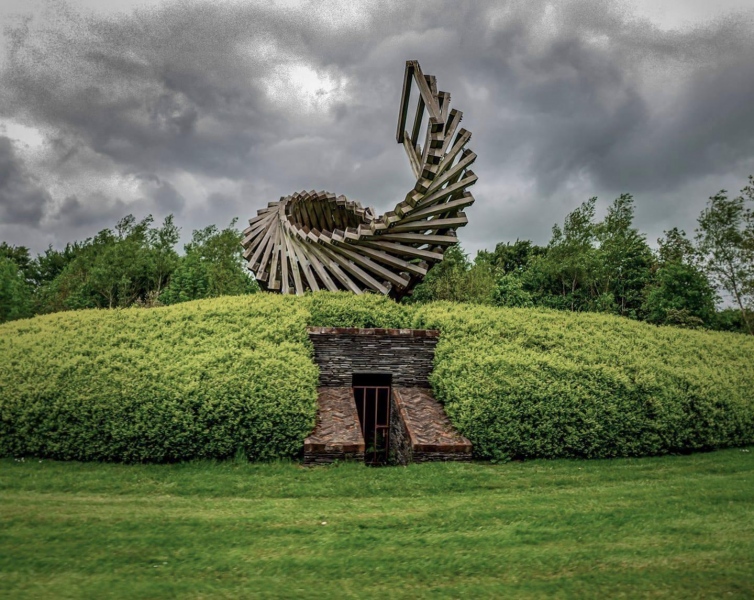 Longsleeper (2009) Oak, steel. Oakfield Park, Raphoe, Co. Donegal '...Longsleeper is made from 17 tons of Oak and appears to perform visual and structural acrobatics! This impressive sculpture has to be seen to be believed. Oakfield Park is renowned for is narrow gauge train and some of the inspiration for the piece comes from the railway. The levers to alter the direction of the track at the &lsquo;points&rsquo; were traditionally secured to a long sleeper. &ldquo;This sense of movement and change is a central idea of the piece&rdquo;, said Locky. Sited on the spiral mound it reveals itself to train passengers in a very dynamic way as they journey around the mound. No two views will be the same, as the straight oak sleepers appear to twist and turn, almost defying gravity. The spiral shape is reminiscent of the double helix of DNA, the genetic instructions for the building of all new life. This birth, or rebirth theme, connects too, to the Biblical story of the awaking of the long sleepers at Ephesus. Locky said, &ldquo;Oak is meant to make an obvious link with the name of the park but the dynamic revolving shape also echoes the spiral leaf arrangement on oak trees. I have visited the park in the past with my own young children and we were all knocked out with the place and especially its beautiful working railway and I tried to inject a sense of playfulness and lightness of touch to this very large and heavy structure&rdquo;. Longsleeper can also be clearly seen in perfect alignment with the middle of Oakfield Park House, 750mtrs away, in keeping with the Georgian design ethos and the gardens. Its circular aspect frames the distant Croaghan Hill, with the ancient burial mound, where it appears to curl up and spin towards the sky'