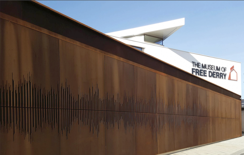 We Shall Overcome (2017) Weathering Steel. Integrated architectural artwork. Museum of Free Derry. Glenfada Park, Derry&nbsp; 'The artwork on the front of this museum shows the sound waveform of the moments on the day of Bloody Sunday in Derry in 1972, when the crowd sings 'We Shall Overcome&rsquo;, a&nbsp;song that had become an anthem for the Civil Rights movement from the late 1950s and early 60s onwards. An emphasis is placed on the surface of the museum having been cut into, along with the suggestion of a huge moment of seismographic shift. It draws also on a number of other ideas, among which are the lines of the wooden fence that would have run along this part of Glenfada Park and in a certain sense draws another line with the infamous &lsquo;rubble barricade&rsquo; that would have crossed Rossville Street on that fateful day. Although it has its focus around this momentous event, it is hoped that it will resonate outside this context and connect, historically and contemporaneously, with a wider international communal struggle and desire for Justice and Civil Rights'